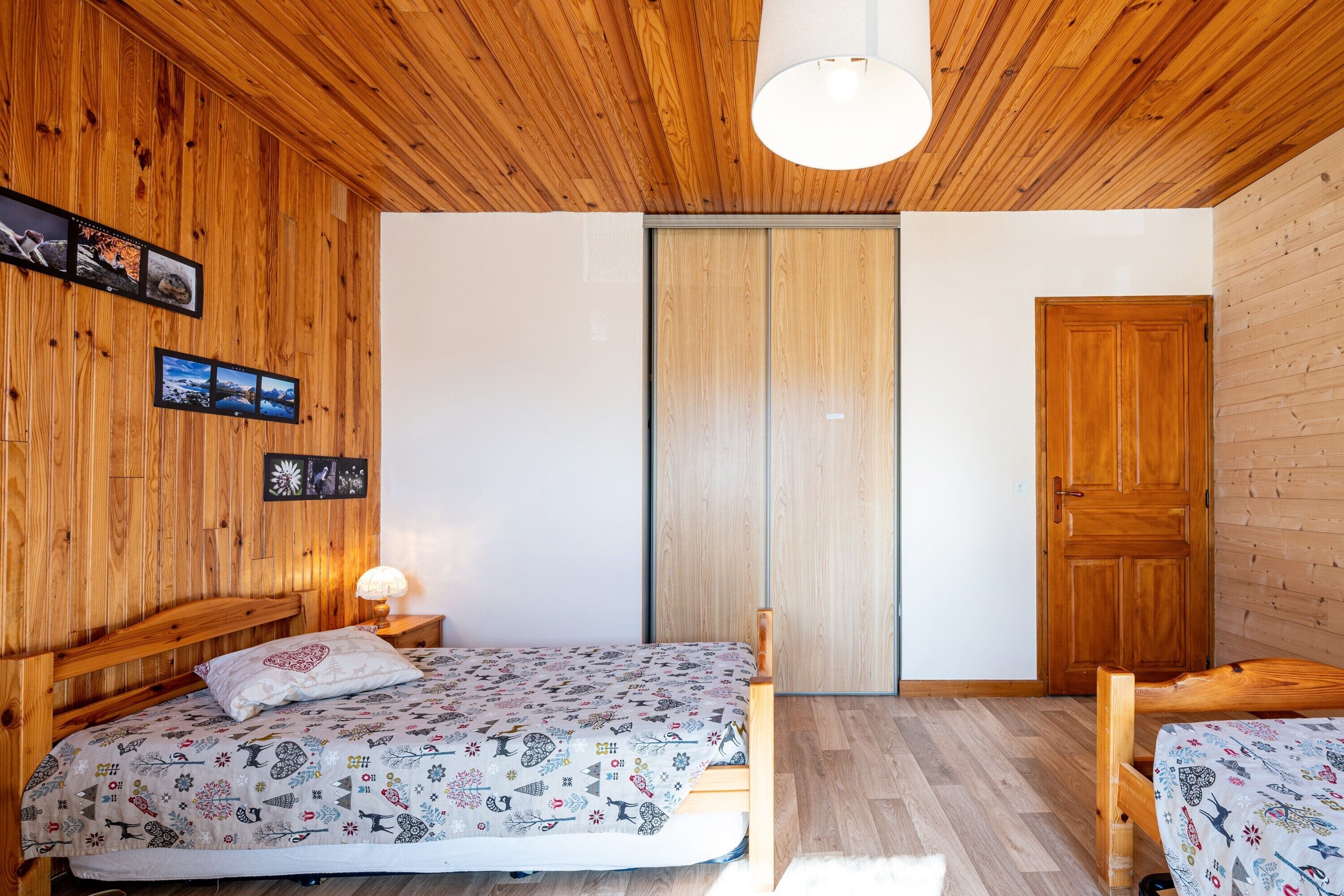 Une chambre à coucher avec un plafond en bois, un lit recouvert d’une couvre-lit à motifs, une table de chevet avec une lampe et une armoire.