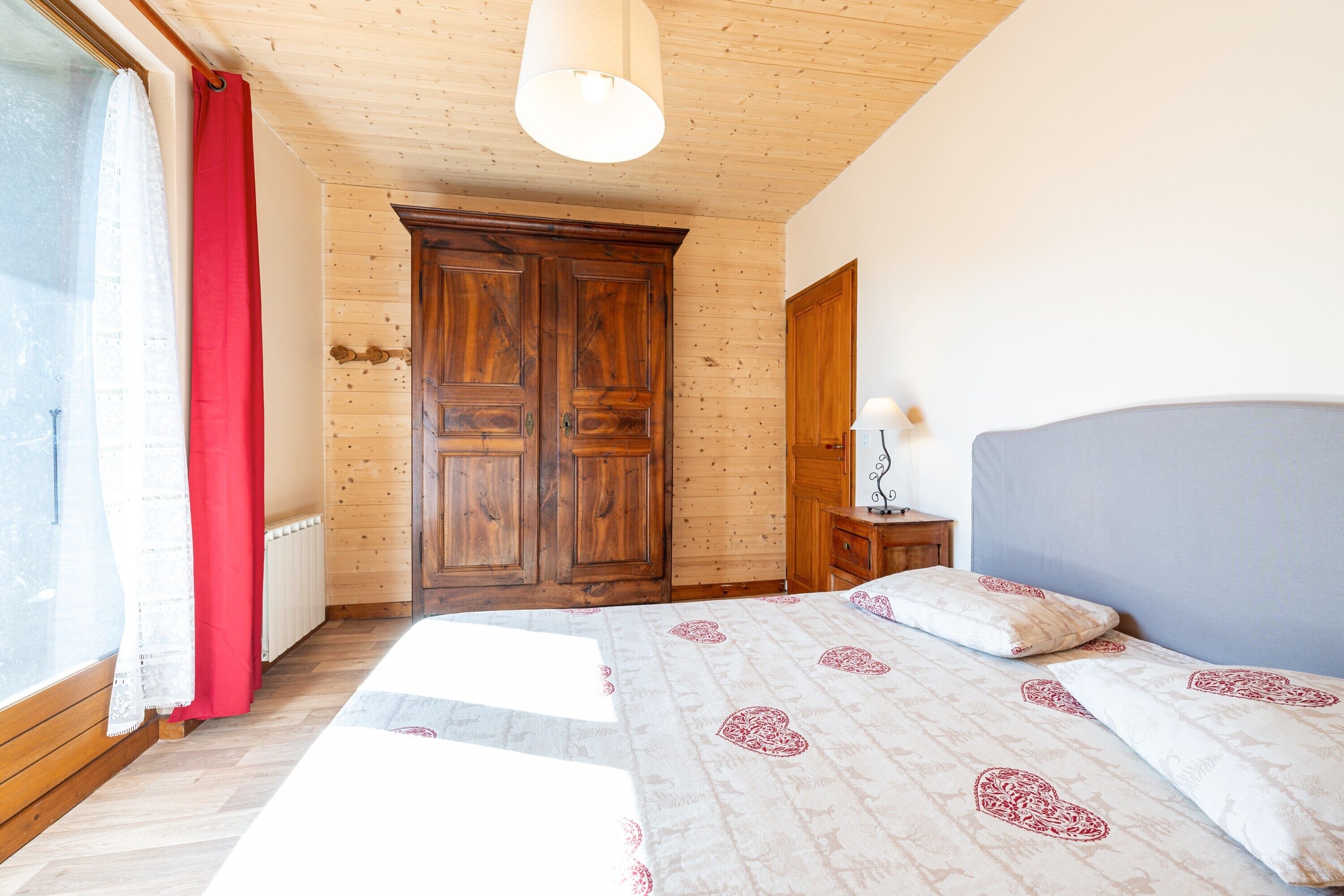 Un dormitorio con un armario de madera, una mesita de noche con lámpara y una cama con ropa de cama estampada.