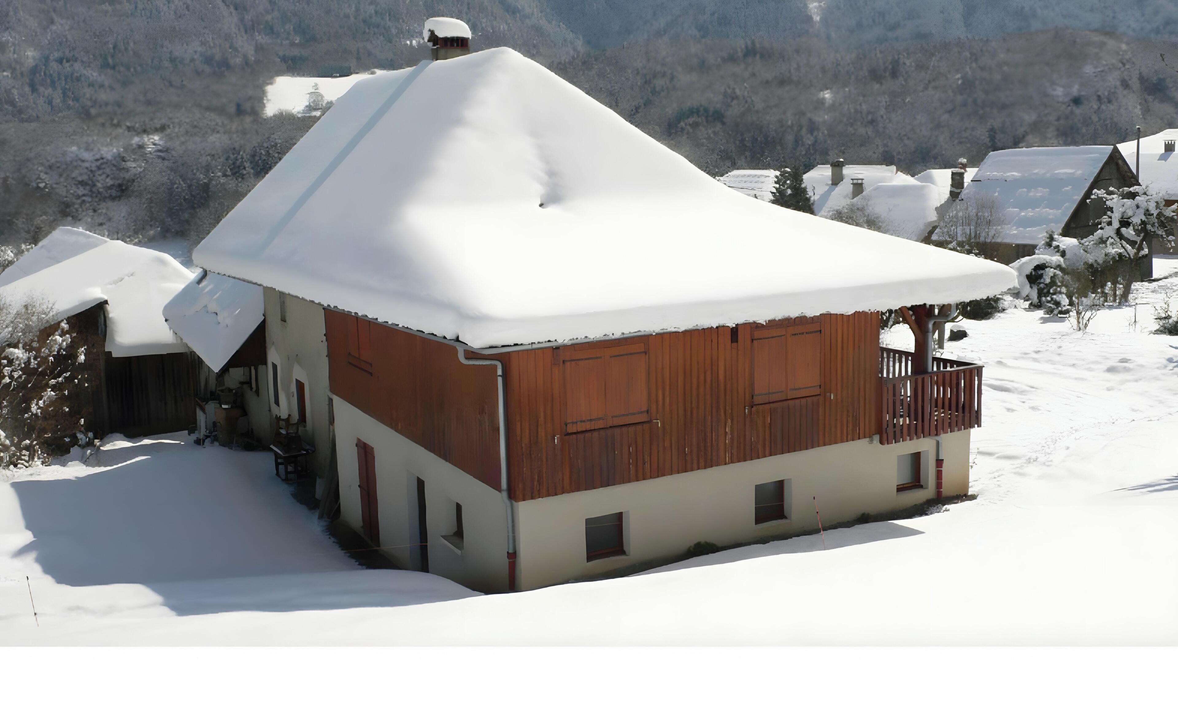 A snow-covered wooden house with a balcony, surrounded by a snowy landscape.