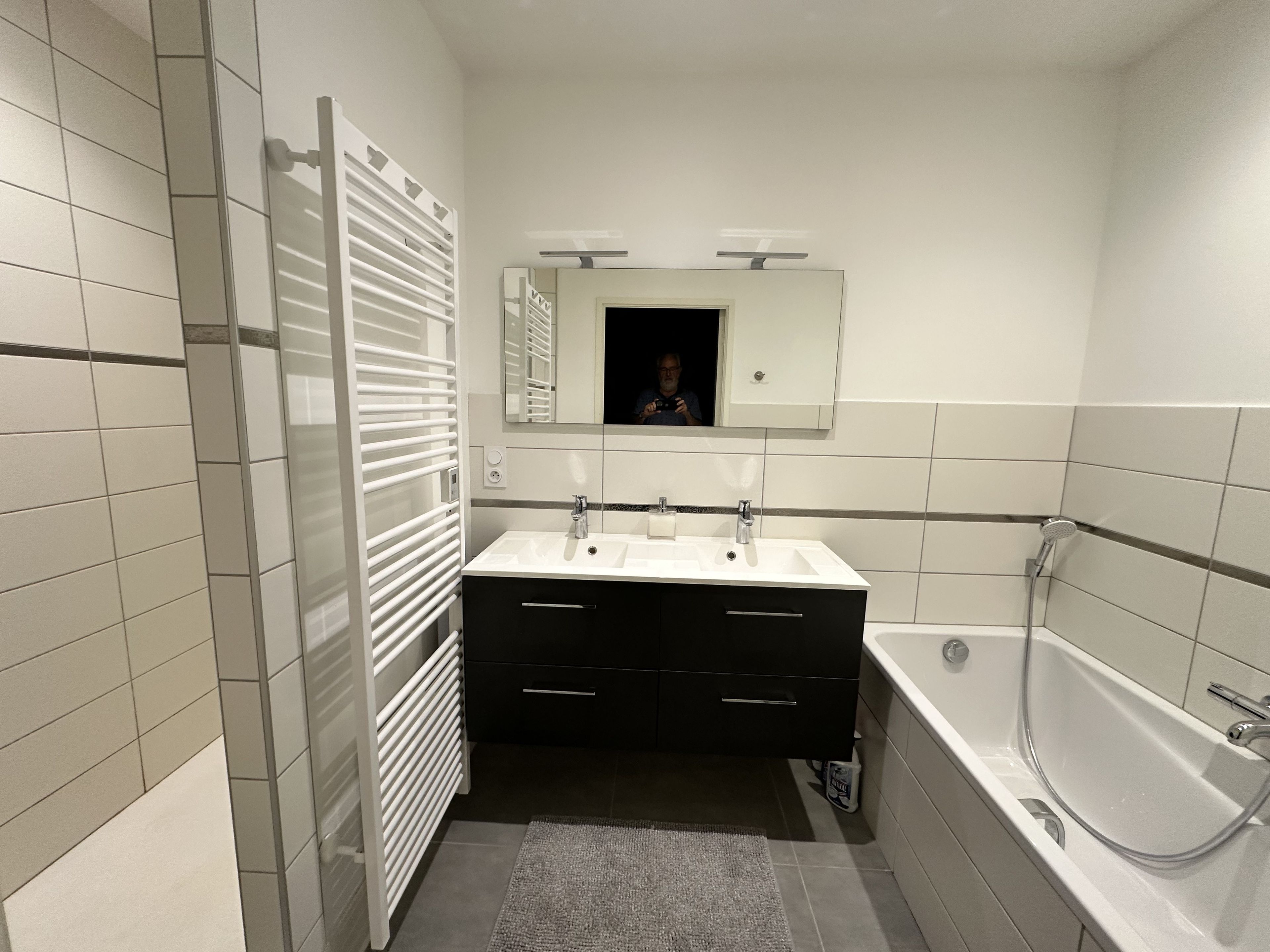 A modern bathroom with a double sink, a bathtub, and a towel rack.