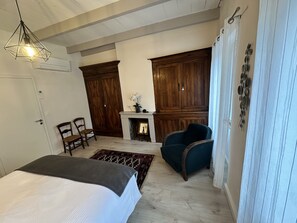 Een kamer met een bed, een open haard, een blauwe fauteuil en houten kasten.