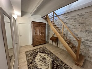 Un couloir avec un escalier en bois, une grande armoire et un tapis à motifs.