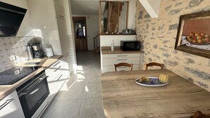 Une cuisine moderne équipée d’un four encastré, d’un four à micro-ondes et d’une machine à café. On y trouve une table à manger avec des chaises et une assiette décorative remplie de fruits.