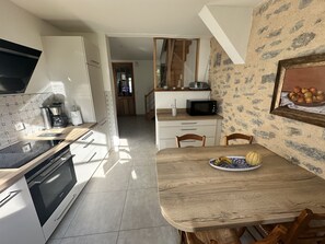 Een moderne keuken met een ingebouwde oven, magnetron en koffiezetapparaat. Er is een eettafel met stoelen en een decoratief schaal fruit.