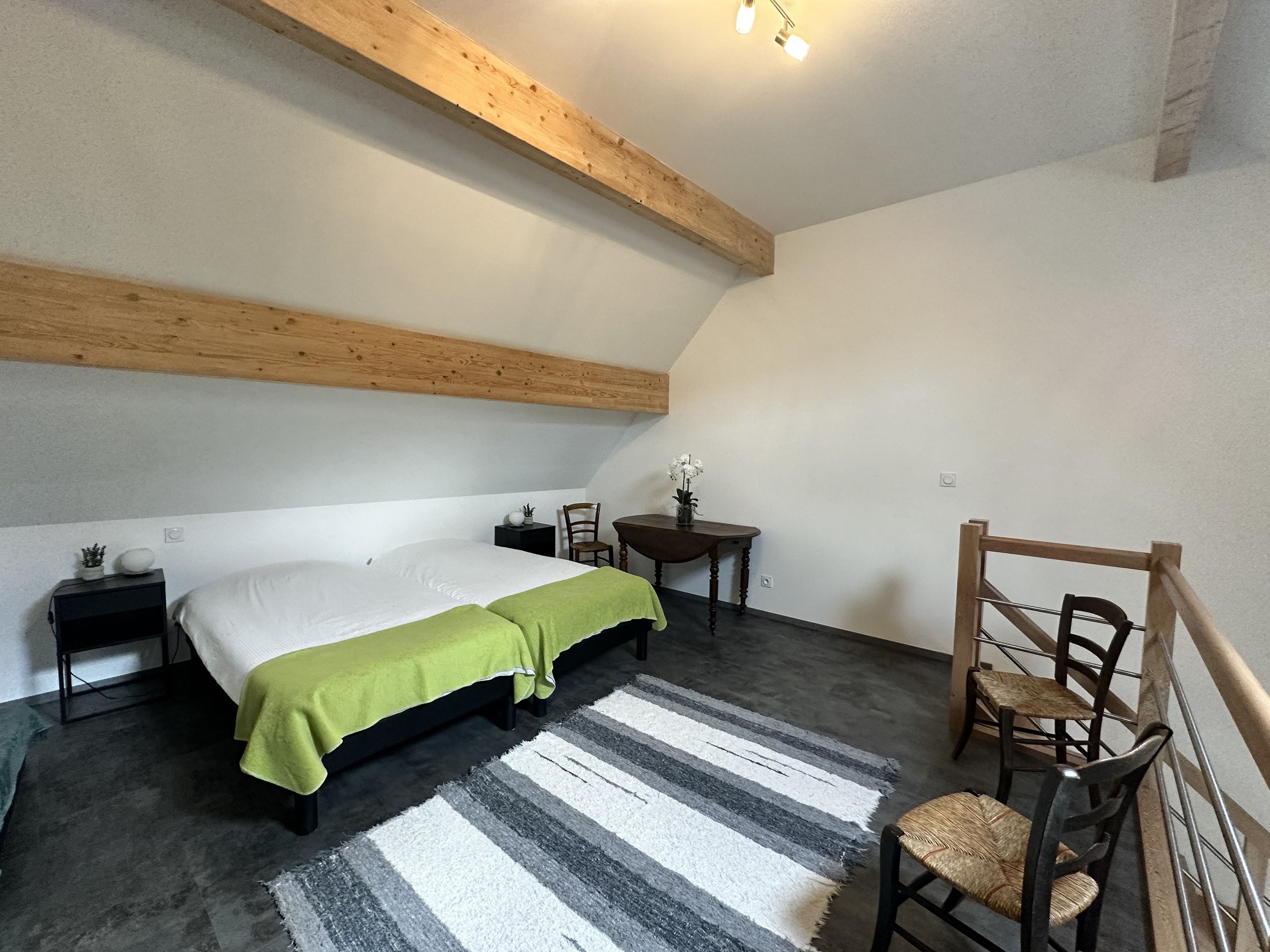 Une chambre à coucher avec un lit, des tables de chevet, une chaise, une petite table avec un vase et un tapis à rayures.