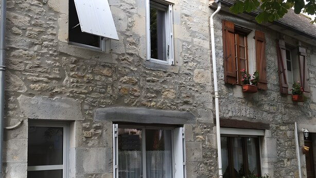 Un bâtiment en pierre doté de nombreuses fenêtres, dont certaines sont pourvues de volets, et d’une porte avec une plaque portant un numéro.