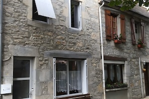 A stone building with multiple windows, some with shutters, and a door with a number plate.