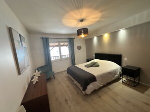 Een slaapkamer met een bed, een bureau, een stoel, een raam met gordijnen en een plafondlamp.