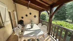 Une terrasse extérieure avec une table et des chaises, un pot de fleurs et une vue sur un jardin.