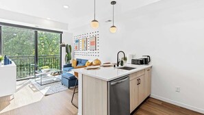 A modern kitchen with a central island, a dining area with a blue sofa, and a large window overlooking greenery. - Luxury 1BD Gym, Rooftop, Street Parking by DT, UMN (Minneapolis)