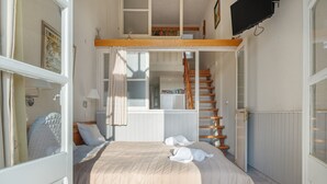 Een slaapkamer met een bed, een raam, een trap en een televisie.