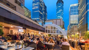An outdoor dining area with tables and chairs, surrounded by tall buildings. - Modern Apt with Rooftop & Skyline Views (Minneapolis)