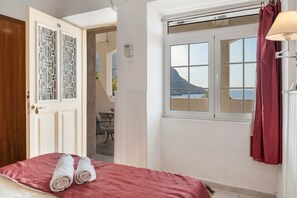 Hotelkamer met een bed, een raam met uitzicht, een deur met decoratieve glaspanelen en een rood gordijn.