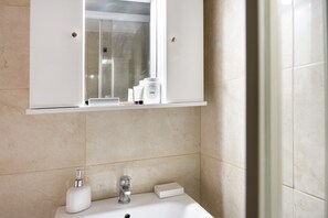 A bathroom with a white sink, a mirror above it, and a shower visible through the glass door.