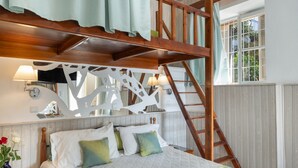 A bedroom with a bed, pillows, a wooden ladder, a wall-mounted TV, and a window with a view of greenery. - Apartment 'Double Studio No 1' with Sea View, Wi-Fi and Air Conditioning (Panormos Kalymnos)