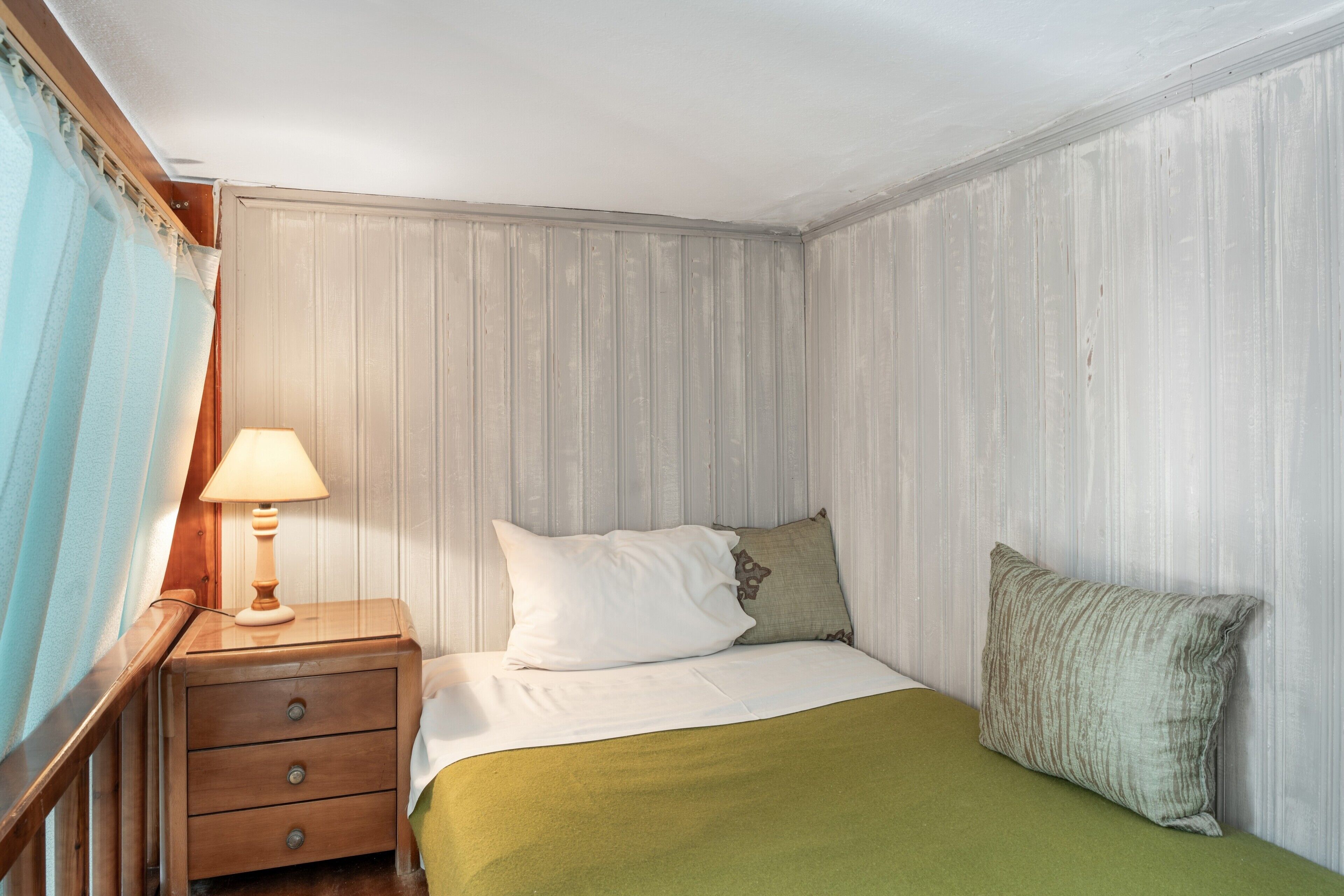 Ein Schlafzimmer mit einem Bett, einem Nachttisch mit Lampe und einem Fenster mit Vorhängen.