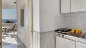 A kitchen with a view of the sea, a dining area with a table and chairs, and a fruit bowl on the counter. - Apartment 'Double Studio No 1' with Sea View, Wi-Fi and Air Conditioning (Panormos Kalymnos)