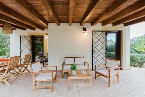 Un espace extérieur aménagé, abrité et doté de mobilier en bois et d’une plante en pot.
