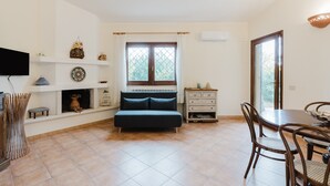 Ein Zimmer mit einem Bett, einem Esstisch mit Stühlen, einem Fernseher, einem Kamin und einem Fenster mit Vorhängen.