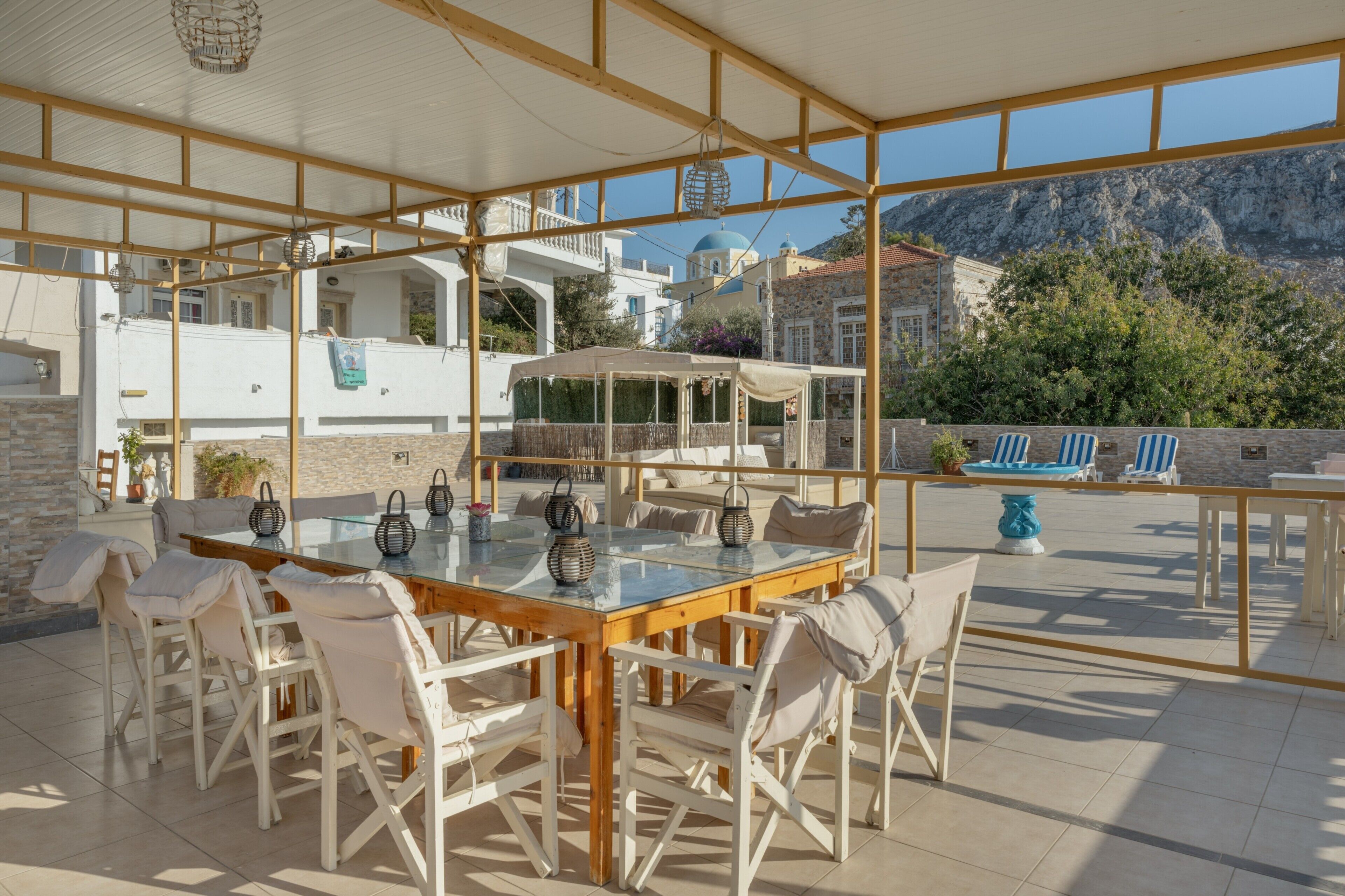 Un área de comedor al aire libre techada con una mesa de vidrio y sillas blancas, con vistas a un paisaje montañoso.