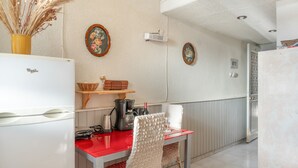Une cuisine compacte équipée d’un réfrigérateur, d’une table à manger avec des chaises, d’une machine à café et d’un panier fixé au mur.