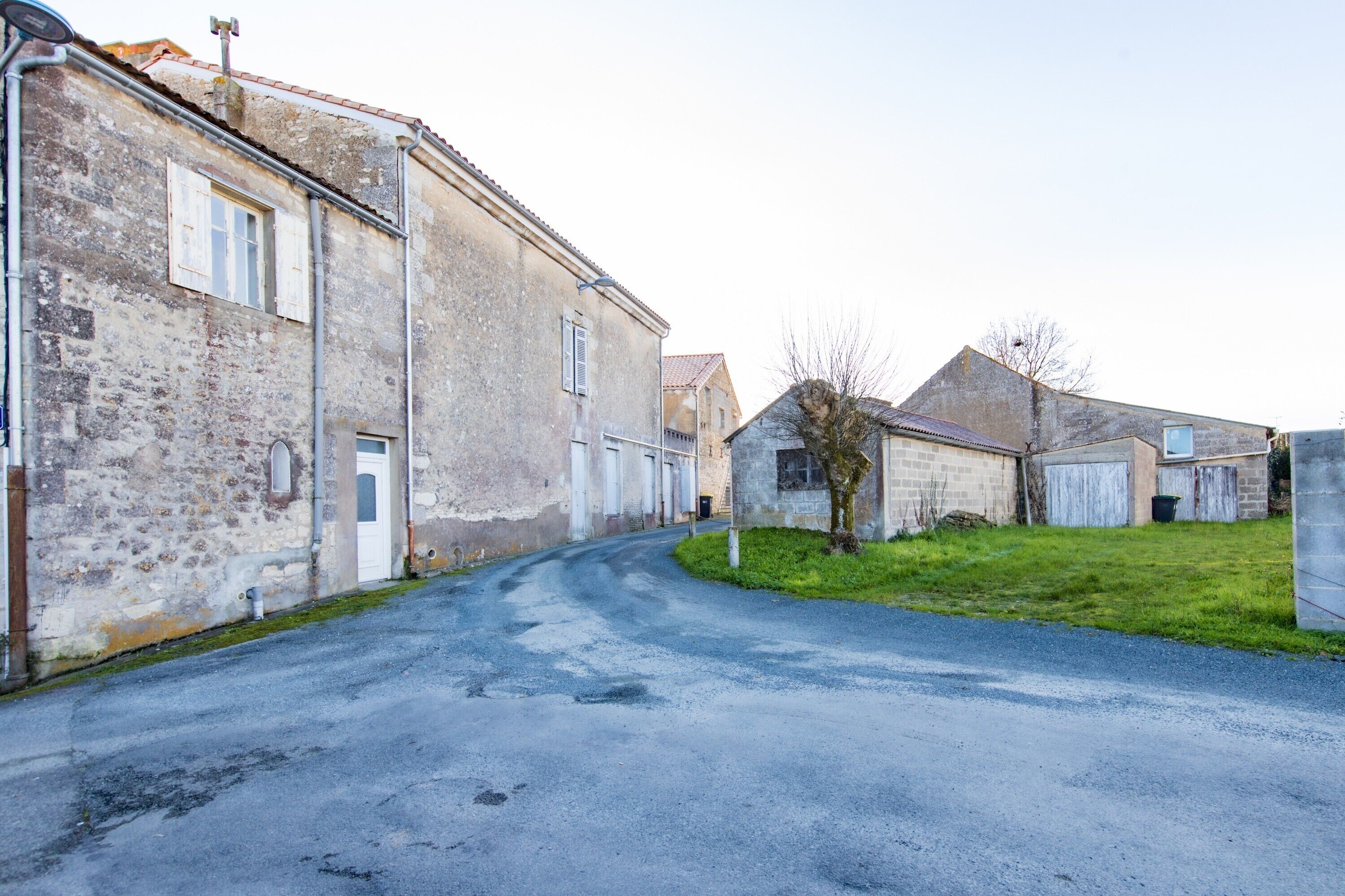 A narrow street lined with old buildings, some with visible doors and windows, leading to a grassy area.