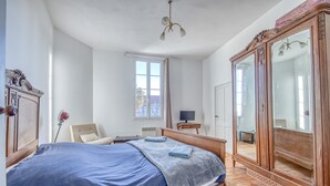 Une chambre à coucher avec un grand lit, une armoire en bois, un bureau avec une chaise et une fenêtre avec des rideaux.