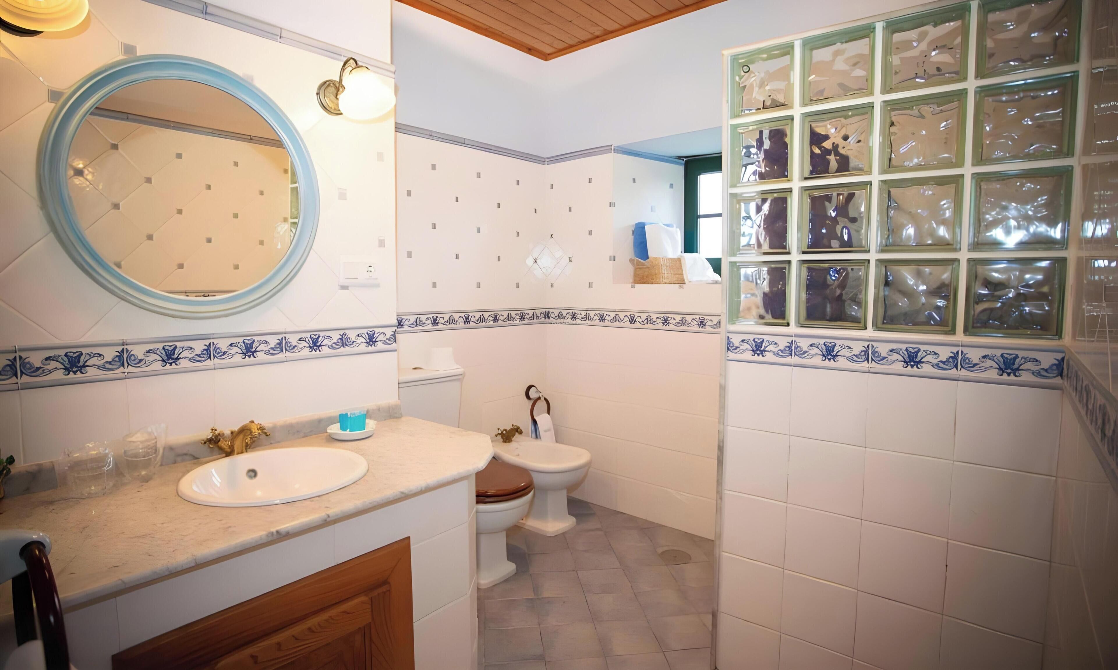 A bathroom with a round mirror, a sink, a toilet, and a wall with decorative tiles.