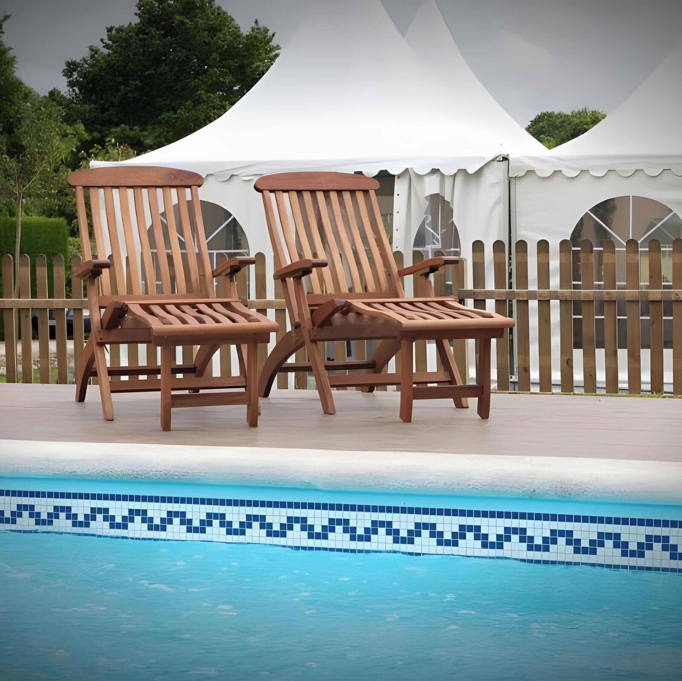 Two wooden lounge chairs by a swimming pool with a tiled edge.