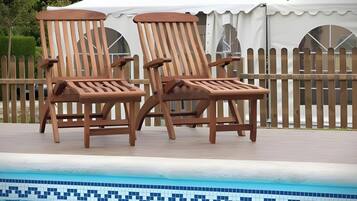 Two wooden lounge chairs by a swimming pool with a tiled edge.