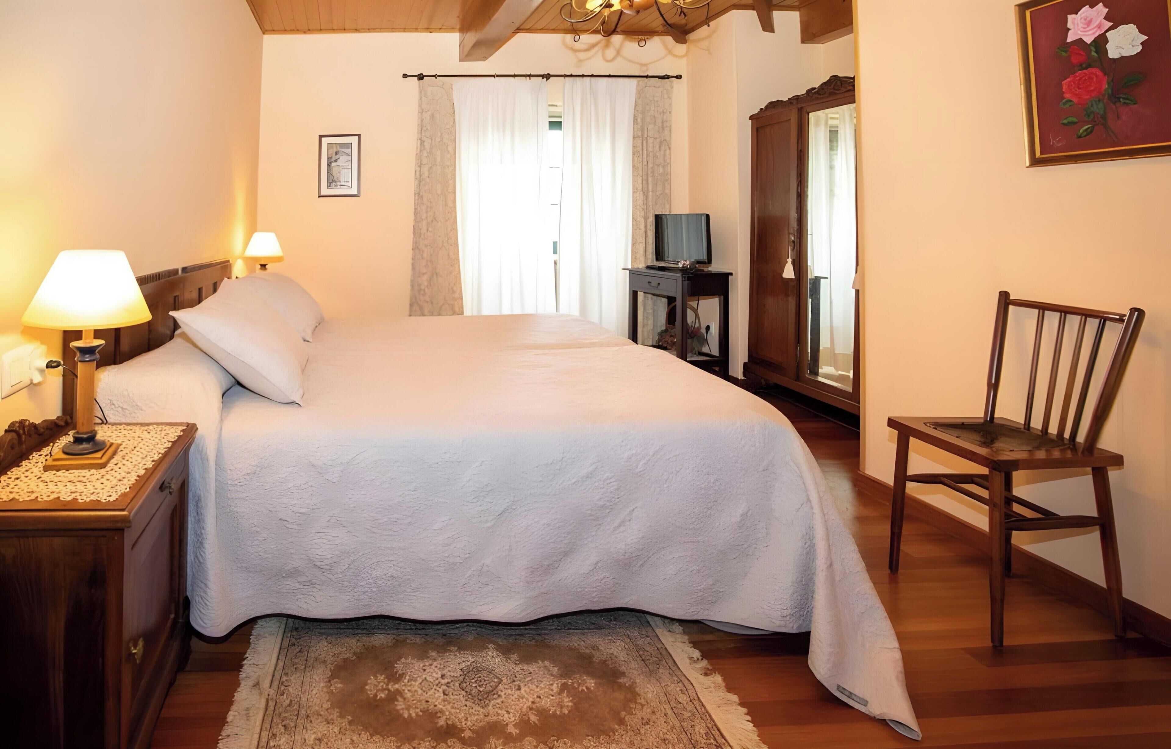 A bedroom with a bed, bedside lamps, a wooden nightstand, a chair, a dresser, a mirror, and a painting on the wall.