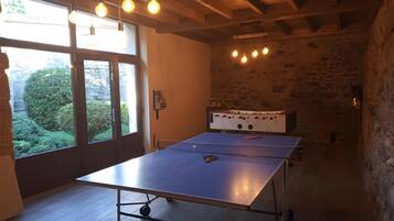 Une table de ping-pong dans une pièce aux murs de pierre, au plafond en bois et à la fenêtre donnant sur un paysage verdoyant.