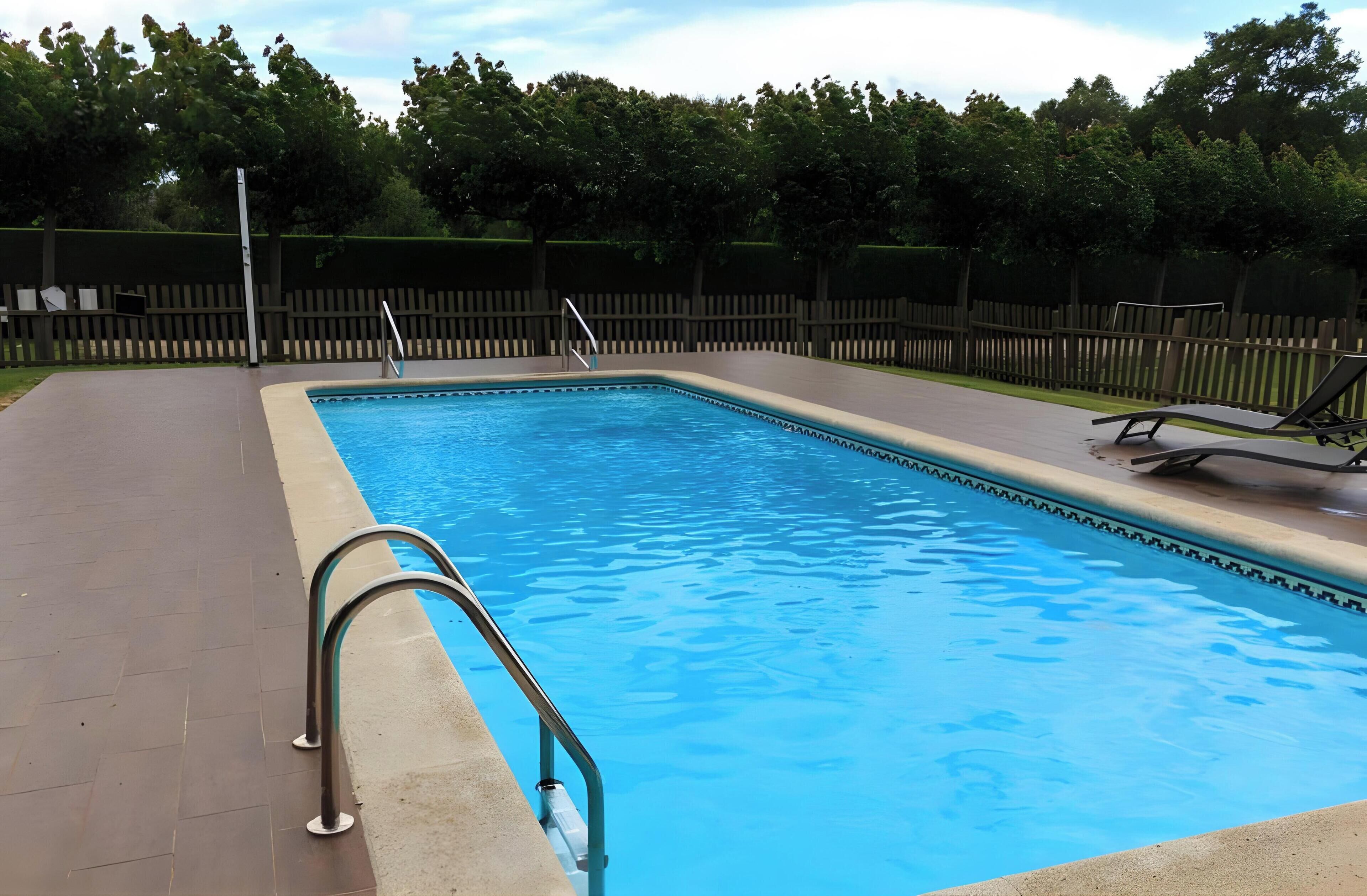 A rectangular swimming pool with a metal ladder and a wooden fence in the background.