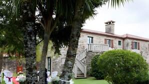 Un edificio de piedra con tejado de tejas rojas, una escalera y un césped bien cuidado con sillas blancas y flores.