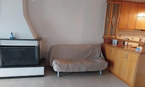 Ein kompakter Wohnbereich mit einer Couch, einem Fernseher, einer Küchenzeile mit Holzschränken und einer gefliesten Spritzwand.
