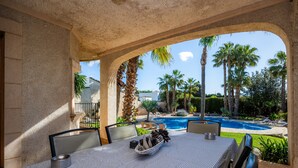 Un área de comedor al aire libre con vista a una piscina y palmeras.