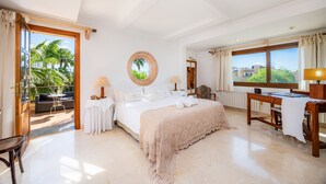 Un dormitorio amplio con una cama grande, un escritorio y vistas a palmeras a través de un ventanal.