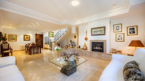 Un amplio salón con una mesa de centro de vidrio, sofás blancos, una chimenea y una escalera.