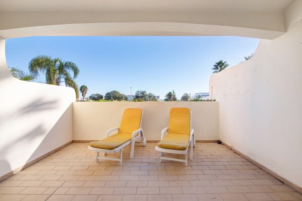 A balcony with two white lounge chairs and a tiled floor.