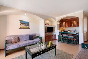 A living room with a sofa, a glass coffee table, and a kitchen area with a dining set.