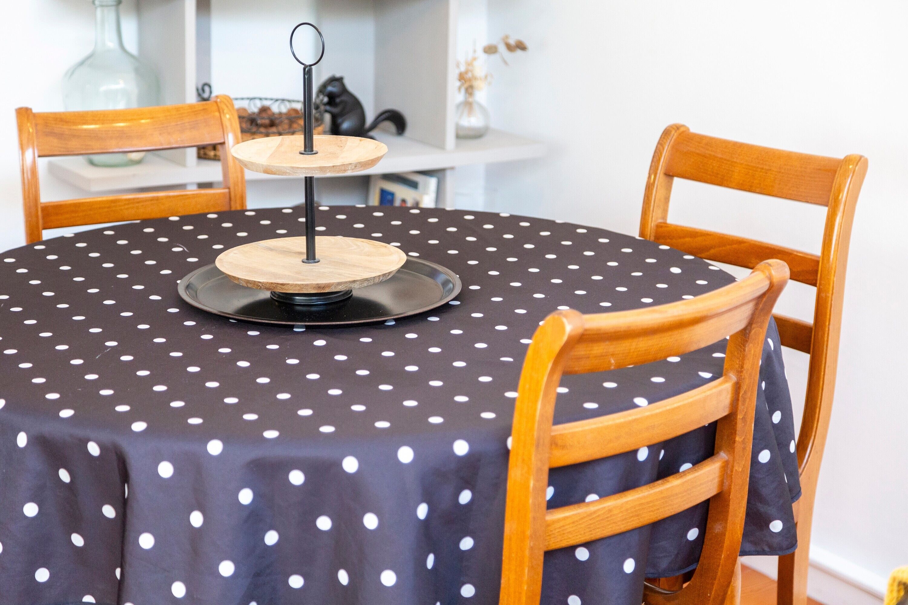 A round table with a polka dot tablecloth, two wooden chairs, and a central wooden stand with a black base.