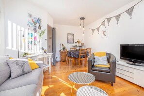 Un salon moderne comprenant un canapé, un fauteuil, un téléviseur, une table à manger et un coin cuisine.