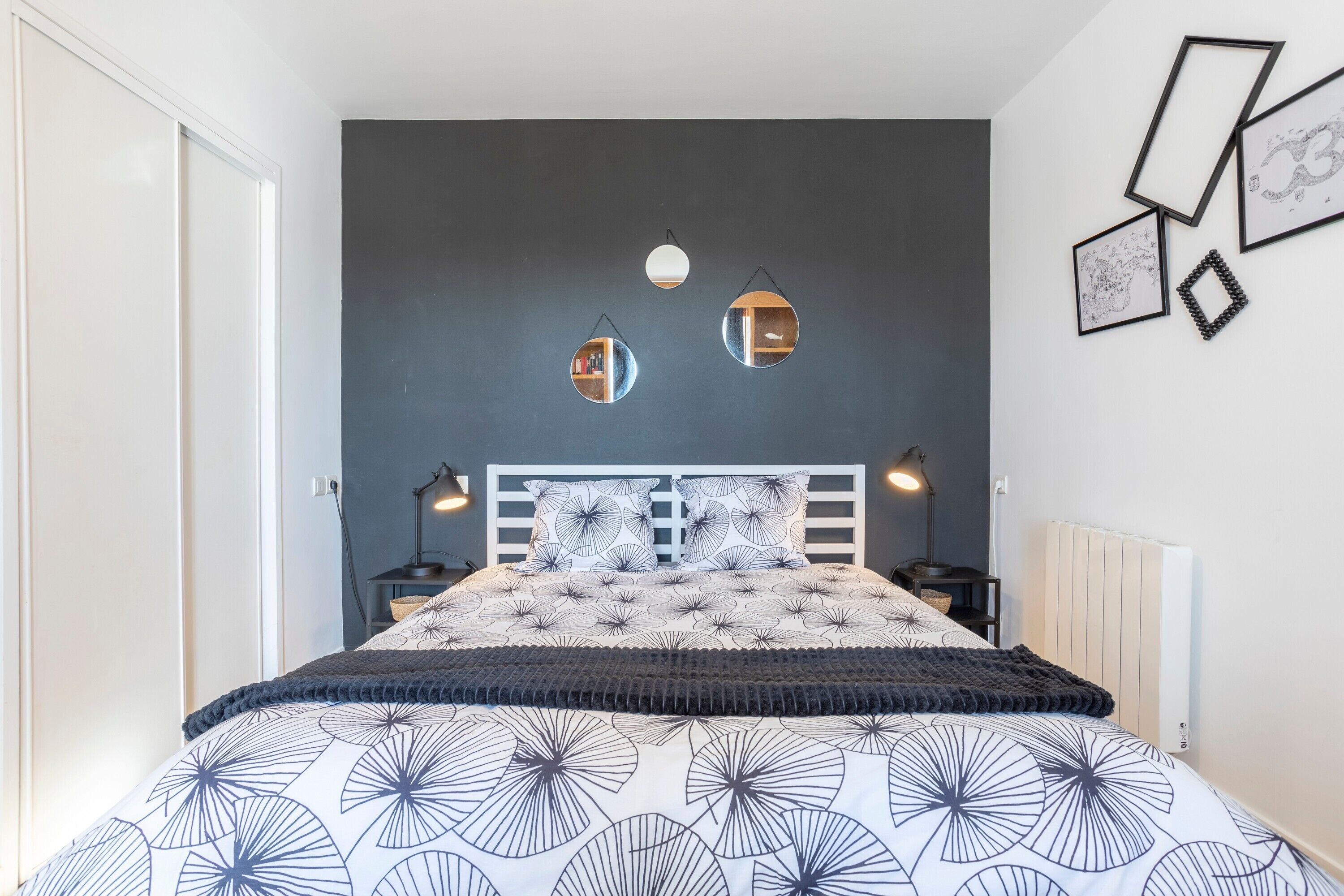 A bedroom with a bed, bedside tables, wall-mounted mirrors, and framed pictures.