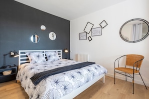 Une chambre à coucher comprenant un lit, des tables de chevet, une chaise, des œuvres d’art murales et un miroir.