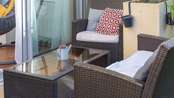 Un canapé en osier avec un coussin, une table basse avec un plateau en verre et une petite plante en pot.