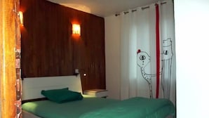 Une chambre à coucher avec une tête de lit en bois, une couvre-lit verte et un mur blanc orné d’un simple dessin.