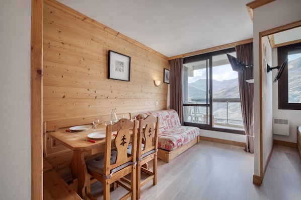 Un intérieur en bois comprenant une table à manger, des chaises, un canapé et une grande fenêtre donnant sur les montagnes.
