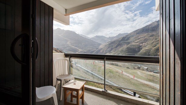 Un balcón con vistas a montañas, una silla y una mesita.