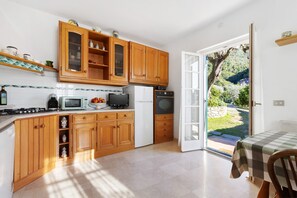 Eine Küche mit Holzausstattung, einer Mikrowelle, einem Herd und einem Kühlschrank. Ein Esstisch mit kariertem Tischläufer steht dort.