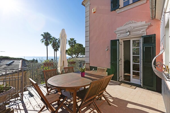 Eine Terrasse mit einem runden Holztisch und Stühlen, einem Blumentopf und Blick auf das Meer.